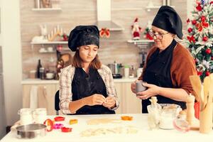 nipote apprendimento per rendere Impasto su Natale giorno a partire dal nonna con grembiule. contento allegro gioioso adolescenziale ragazza porzione anziano donna preparazione dolce biscotti per celebrare inverno vacanze. foto