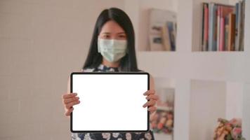 donna asiatica che indossa una maschera con in mano un tablet di fronte allo schermo anteriore per un messaggio di protezione contro il virus corona o covid-19. foto