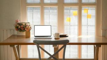 colpo ritagliato del posto di lavoro classico con un laptop, una tazza di caffè e un fermo su un tavolo di legno vicino alla finestra. foto