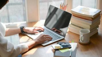 da vicino, la mano della ragazza sta usando un laptop su una scrivania di legno in ufficio con una bella illuminazione. foto
