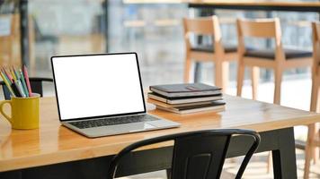 colpo ritagliato di laptop con notebook e fermo su una scrivania di legno in un ufficio moderno. foto