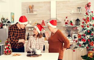 anziano uomo festeggiare Natale con contento nipote dando sua regalo scatola indossare Santa cappello. contento amorevole nonni festeggiare inverno vacanze e relazione con nipotina nel casa con x-mas decorazione. foto