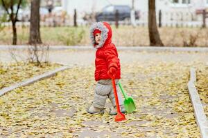 un' piccolo ragazzo con un' rastrello e un' pala passeggiate nel il parco foto
