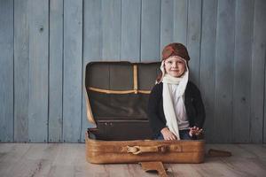 bambino felice in cappello pilota che gioca con la vecchia valigia. infanzia. fantasia, immaginazione. vacanza