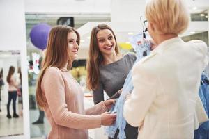 giovani belle donne al mercato settimanale del panno. il responsabile del negozio aiuta l'acquirente. migliori amici che condividono il tempo libero divertendosi e facendo shopping foto