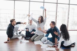 giovani creativi in un ufficio moderno. gruppo di giovani uomini d'affari stanno lavorando insieme al computer portatile. liberi professionisti seduti per terra. cooperazione aziendale successo. concetto di lavoro di squadra foto