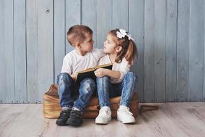 pronto per il grande viaggio. felice bambina e ragazzo che leggono un libro interessante che trasporta una grande valigetta e sorridono. concetto di viaggio, libertà e immaginazione foto