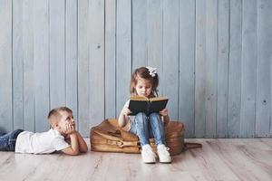 pronto per il grande viaggio. felice bambina e ragazzo che leggono un libro interessante che trasporta una grande valigetta e sorridono. concetto di viaggio, libertà e immaginazione foto