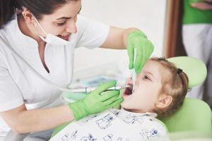 controllo dei denti presso l'ufficio del dentista. dentista che esamina i denti delle ragazze sulla sedia del dentista foto