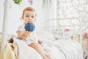 concetto di infanzia. bambina in abito carino ubicazione a letto giocando con i giocattoli da casa. cameretta bianca vintage foto