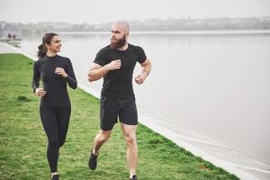 coppia fare jogging e correre all'aperto nel parco vicino all'acqua. giovane uomo e donna barbuti che si esercitano insieme al mattino foto