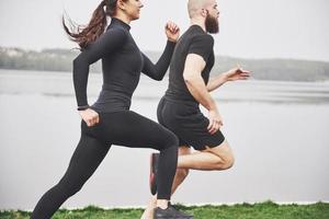 coppia fare jogging e correre all'aperto nel parco vicino all'acqua. giovane uomo e donna barbuti che si esercitano insieme al mattino foto