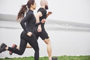 coppia fare jogging e correre all'aperto nel parco vicino all'acqua. giovane uomo e donna barbuti che si esercitano insieme al mattino foto