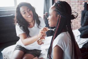 due belle ragazze africane in pigiameria sorridenti sedute sul letto a casa si sono svegliate la mattina in una giornata di sole. foto