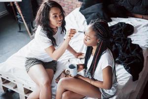 due belle ragazze africane in pigiameria sorridenti sedute sul letto a casa si sono svegliate la mattina in una giornata di sole. foto
