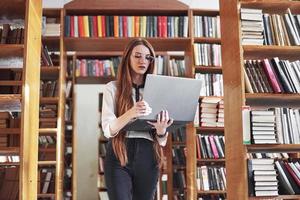 la giovane bella donna è una studentessa in una biblioteca con il suo laptop foto