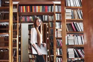 la giovane bella donna è una studentessa in una biblioteca con il suo laptop foto