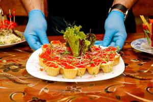 Uomini mani servendo su il tavolo piatto con caviale nel tartellette e erbe aromatiche foto