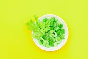 fresco tritato sedano pezzi con acqua gocce nel bianca ciotola su giallo sfondo. vegano e vegetariano cultura. crudo cibo. salutare dieta con negativo caloria soddisfare foto