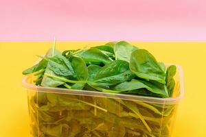 fresco bambino spinaci le foglie nel trasparente plastica pacchetto su giallo sfondo. vegano e vegetariano cultura. crudo cibo, verde le foglie. salutare dieta foto