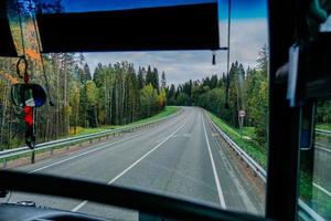 vista della strada e del bosco autunnale attraverso il finestrino dell'autobus. viaggio su strada foto