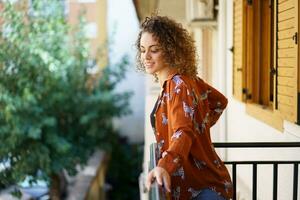 contento giovane donna nel casuale indossare con Riccio capelli in piedi su balcone foto