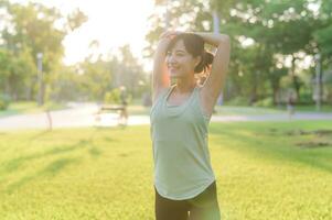 femmina pareggiatore. in forma giovane asiatico donna con verde abbigliamento sportivo allungamento muscolo nel parco prima in esecuzione e godendo un' salutare all'aperto. fitness corridore ragazza nel pubblico parco. benessere essere concetto foto