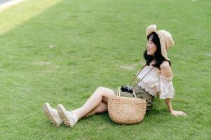 ritratto di asiatico giovane donna viaggiatore con tessitura cappello e cestino e un' telecamera su verde pubblico parco natura sfondo. viaggio viaggio stile di vita, mondo viaggio esploratore o Asia estate turismo concetto. foto