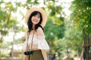 ritratto di asiatico giovane donna viaggiatore con tessitura cappello e cestino e un' telecamera su verde pubblico parco natura sfondo. viaggio viaggio stile di vita, mondo viaggio esploratore o Asia estate turismo concetto. foto