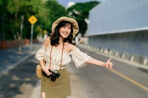 ritratto di asiatico giovane donna viaggiatore con tessitura cappello e cestino e un' telecamera agitando mano per amico di il strada. viaggio viaggio stile di vita, mondo viaggio esploratore o Asia estate turismo concetto. foto