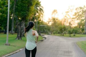 in forma asiatico giovane donna jogging nel parco sorridente contento in esecuzione e godendo un' salutare all'aperto stile di vita. femmina pareggiatore. fitness corridore ragazza nel pubblico parco. salutare stile di vita e benessere essere concetto foto