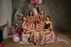 donne nel sexy biancheria intima e sposa nel velo avendo divertimento durante Addio al nubilato, seduta su letto, sorridente, Tenere palloncini. studio con nuovo anno decorazioni. foto