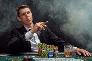 bello emotivo uomo è giocando poker seduta a il tavolo nel casinò contro un' bianca riflettore. foto