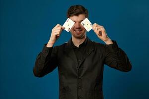 novizio nel poker, nel nero veste e camicia. Tenere Due giocando carte mentre in posa contro blu studio sfondo. gioco d'azzardo, casinò. avvicinamento. foto