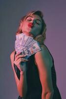 bionda ragazza nel nero elegante vestito Tenere alcuni i soldi, in posa contro colorato sfondo. gioco d'azzardo intrattenimento, poker, casinò. avvicinamento. foto