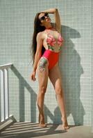 ritratto di un' donna avendo riposo nel un' ricreazione centro o Hotel con un' nuoto piscina. vestito nel un' colorato costume da bagno e occhiali da sole. foto