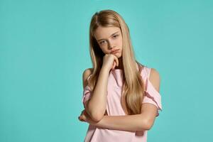 studio ritratto di un' bellissimo ragazza bionda adolescente nel un' rosa maglietta in posa al di sopra di un' blu sfondo. foto