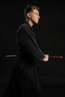 kendo guru indossare nel un' tradizionale giapponese chimono è praticante marziale arte con il shinai bambù spada contro un' nero studio sfondo. foto