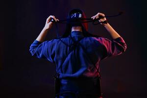 vicino su sparo, kendo combattente indossare nel un armatura e tradizionale chimono è legatura il allacciatura su il suo casco in piedi indietro contro un' nero sfondo. foto