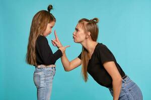 mamma e figlia con un' divertente acconciature, vestito nel nero camicie e blu denim jeans siamo in posa contro un' blu studio sfondo. avvicinamento sparo. foto