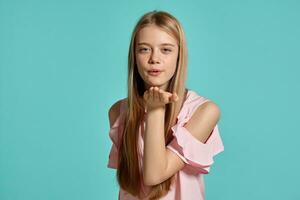 studio ritratto di un' bellissimo ragazza bionda adolescente nel un' rosa maglietta in posa al di sopra di un' blu sfondo. foto