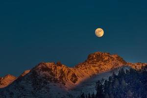 luna piena al tramonto sulle montagne d'inverno foto