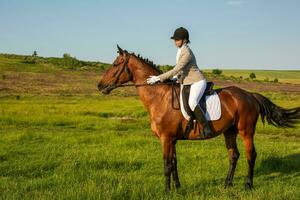 giovane donna equitazione un' cavallo su il verde campo foto