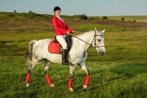 giovane donna cavaliere, indossare rosso redingote e bianca calzoni, con sua cavallo nel sera tramonto luce. foto