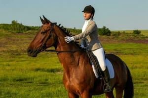 giovane donna equitazione un' cavallo su il verde campo foto