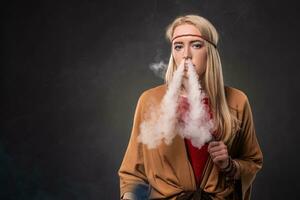 ritratto di sexy giovane fricchettone fumo vaping ragazza. il donna è vestito nel il stile di un' boho. vapore concetto. vaping sigaretta elettronica. foto