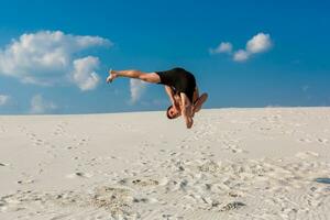 ritratto di giovane parkour uomo fare Flip o capriola su il sabbia. foto