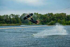 esperto wakeboard ciclista salto e Filatura nel aria Tenere su per trainare cavo foto