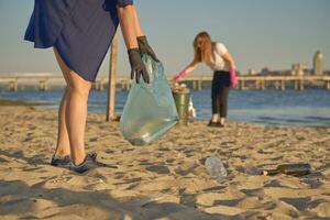 giovane volontari nel nero guanti siamo a piedi con spazzatura borse lungo un' sporco spiaggia di il fiume e pulizia su spazzatura. persone e ecologia. avvicinamento. foto