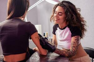 sorridente femmina tatuaggio artista la creazione di elegante lettering su braccio di donna foto